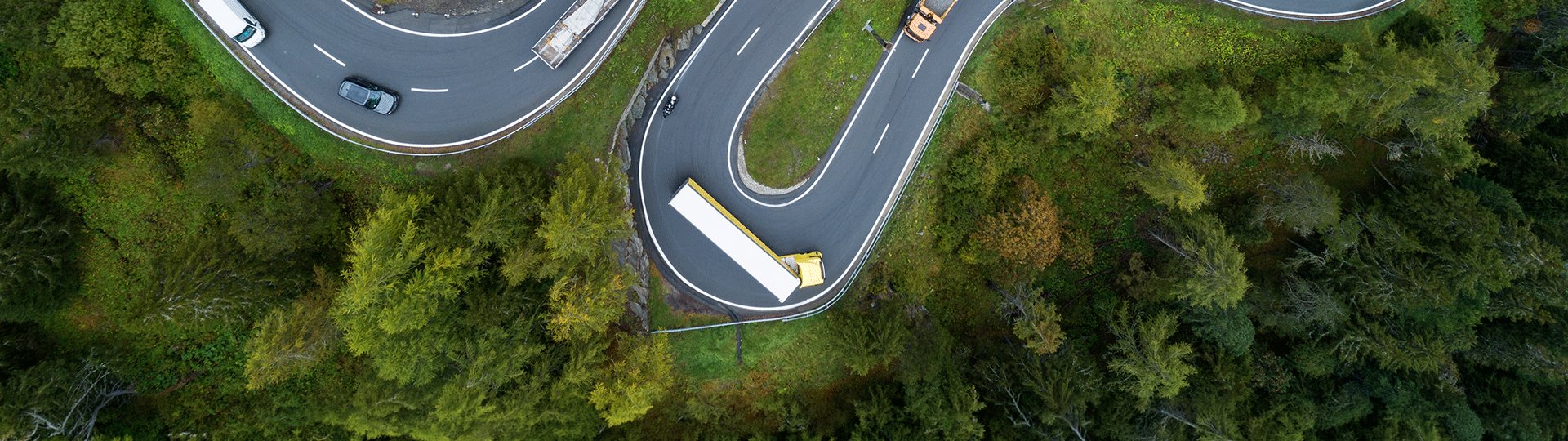 Versicherung für Ihren Mitsubishi abschließen Mehrere Autos fahren auf einer kurvenreichen Straße durch einen dicht bewaldeten Abschnitt.