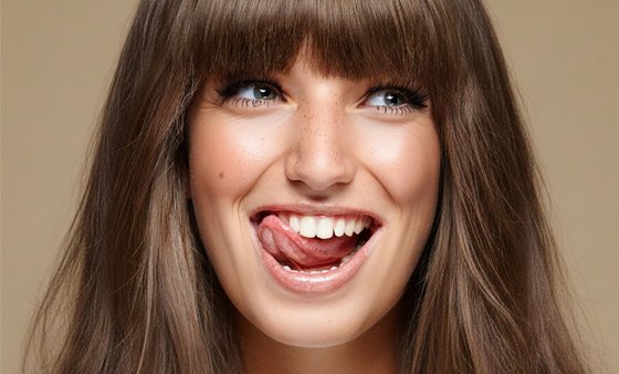 Eine Frau lächelt und zeigt dabei ihre Zähne. Sie leckt sich mit der Zunge über die oberen Zähne.