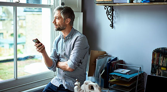AXA - Mann zu Hause mit Handy schaut in den Garten