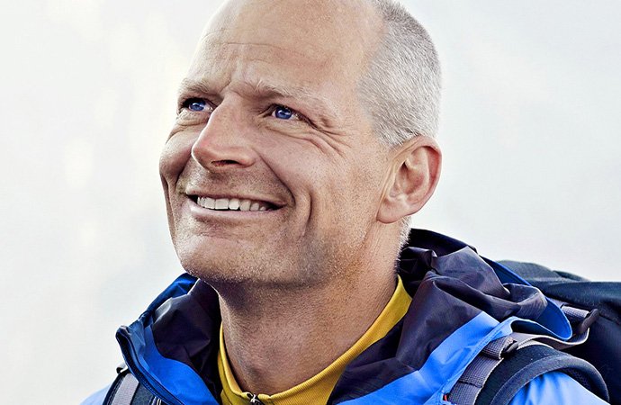 Älterer Mann mit grauen Haaren und Outdoorjacke lächelt zufrieden beim Wandern und blickt nach oben.