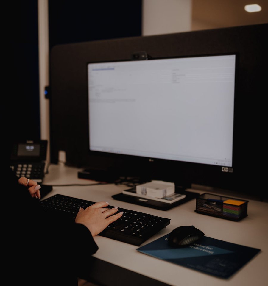 Kontaktieren Sie uns Hände einer Person bedienen eine Tastatur an einem Büroarbeitsplatz mit Monitor, Telefon, Maus und Notizmaterial.