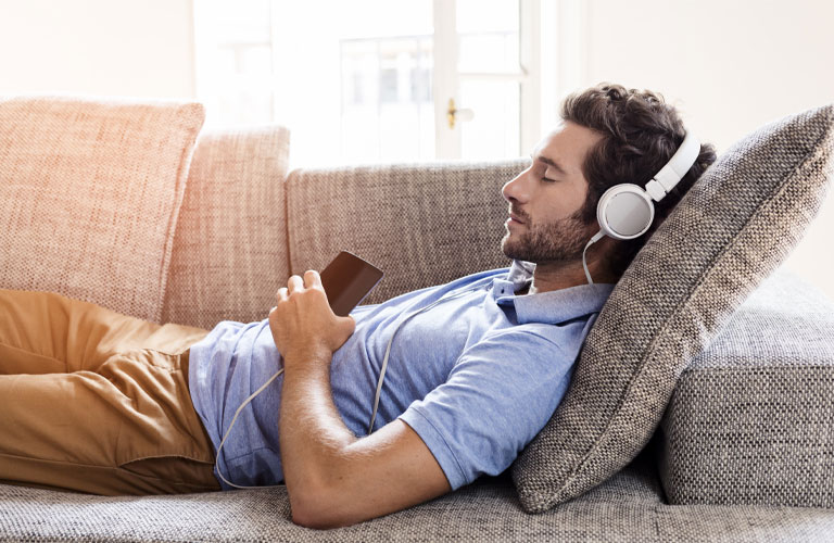 Mann-liegt-auf-sofa-und-hoert-musik-ueber-kopfhoerer-768x500.jpg Mann-liegt-auf-sofa-und-hoert-musik-ueber-kopfhoerer-768x500.jpg