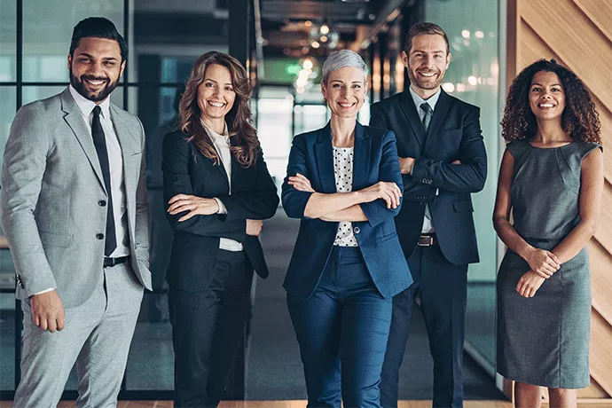 F&uuml;nf Gesch&auml;ftsleute unterschiedlicher Altersgruppen stehen selbstbewusst nebeneinander in einem modernen B&uuml;ro und l&auml;cheln in die Kamera.