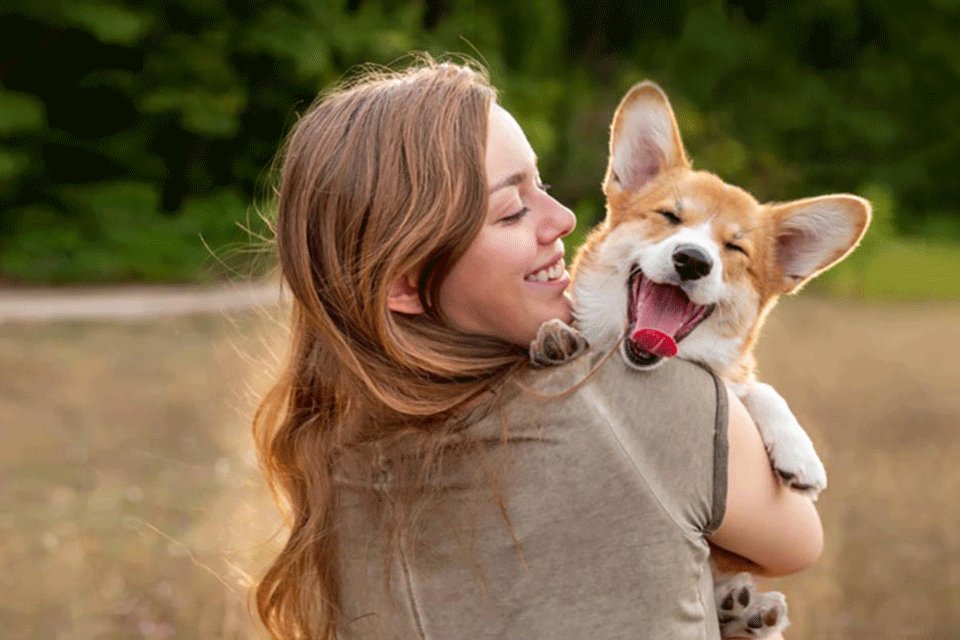 Junge Frau umarmt einen fr&ouml;hlichen Hund im Park. Der Hund tr&auml;gt eine Leine, streckt die Zunge heraus und wirkt verspielt und zufrieden.
