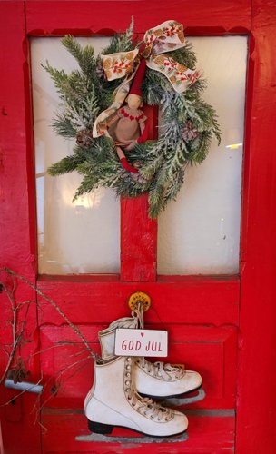 Eine Rote T&uuml;r an der ein Weihnachtskranz h&auml;ngt, sowie wei&szlig;e Schlittschuhe.