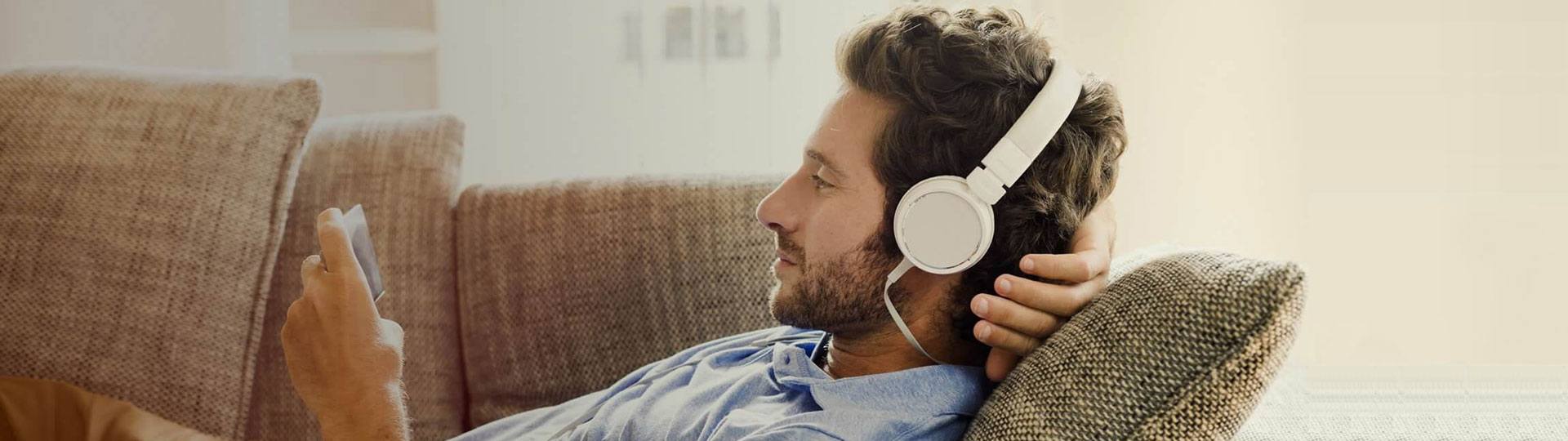 Mann liegt entspannt auf dem Sofa und hört Musik