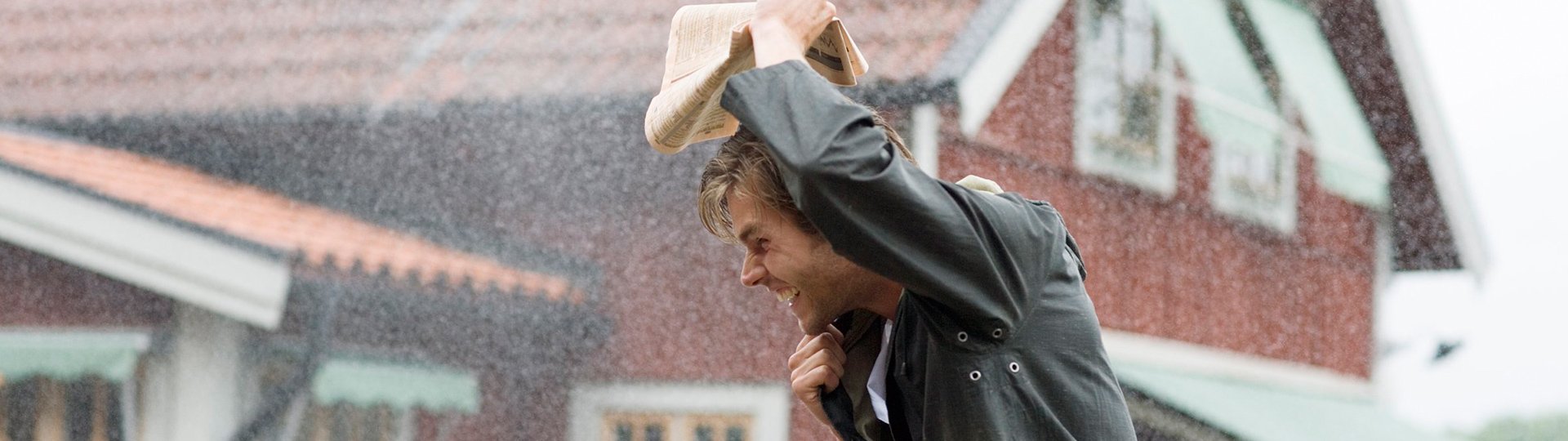 Mann läuft durch den Regen und hält sich eine Zeitung über den Kopf