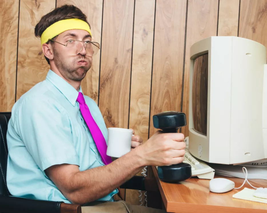 Sportlicher Mann situt vor dem Computer mit einer Hantel und einem Kafee in der Hand